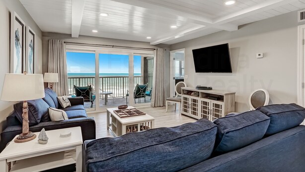 A modern living room with a sofa, coffee table, and TV. There is a balcony with a view of the sea. - Fully Renovated oceanfront getaway with a modern coastal feel and amazing ocean views! (Fernandina Beach)