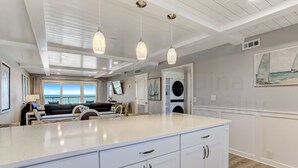 A modern kitchen with a large island, pendant lights, and a view of the ocean through the windows. - Fully Renovated oceanfront getaway with a modern coastal feel and amazing ocean views! (Fernandina Beach)