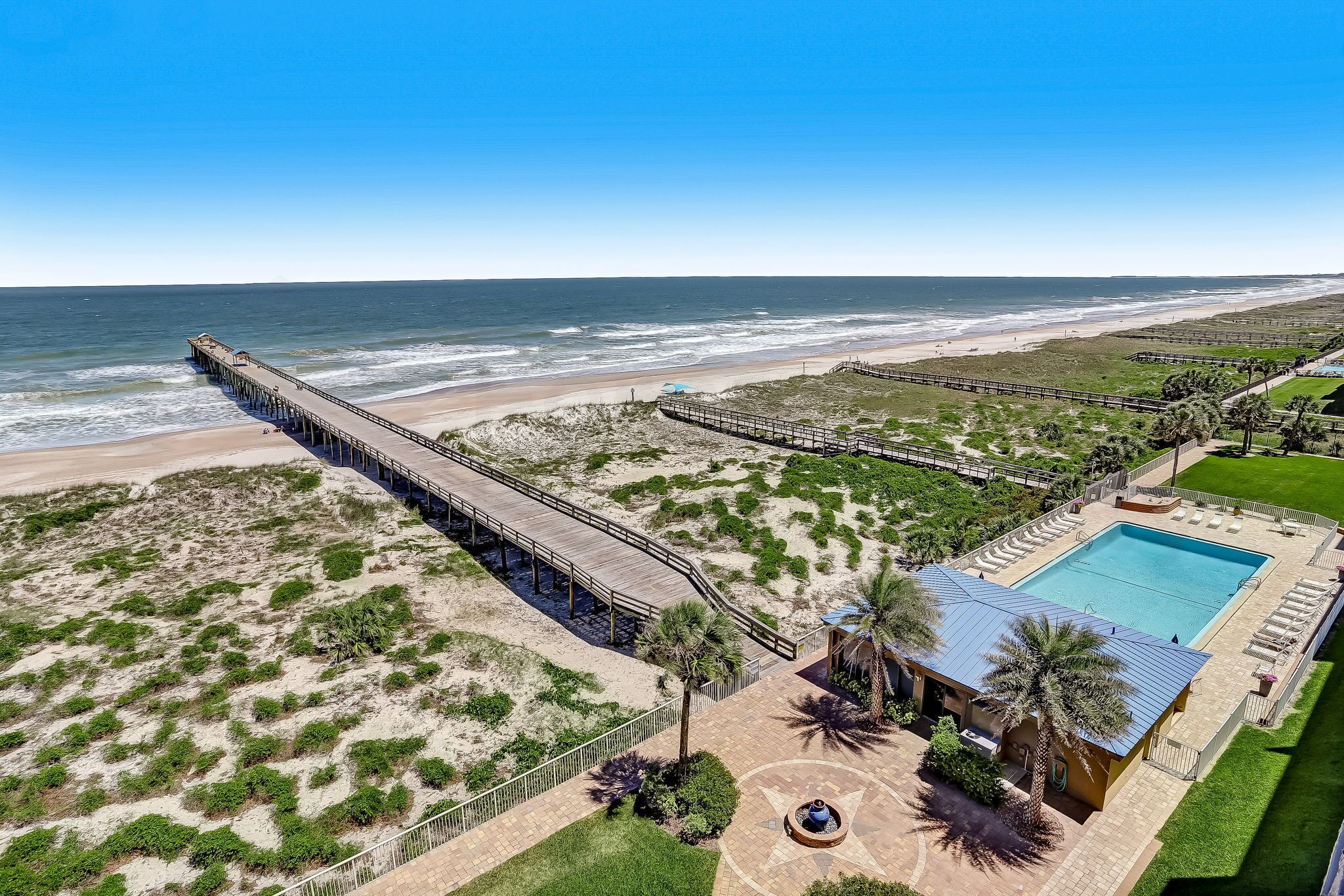 Een pand aan het strand met een lange steiger, een zwembad en een aangelegde tuin met palmbomen.