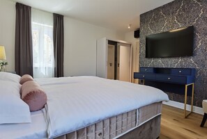 Une chambre à coucher moderne avec un grand lit, une armoire, un téléviseur fixé au mur et un papier peint à motifs.