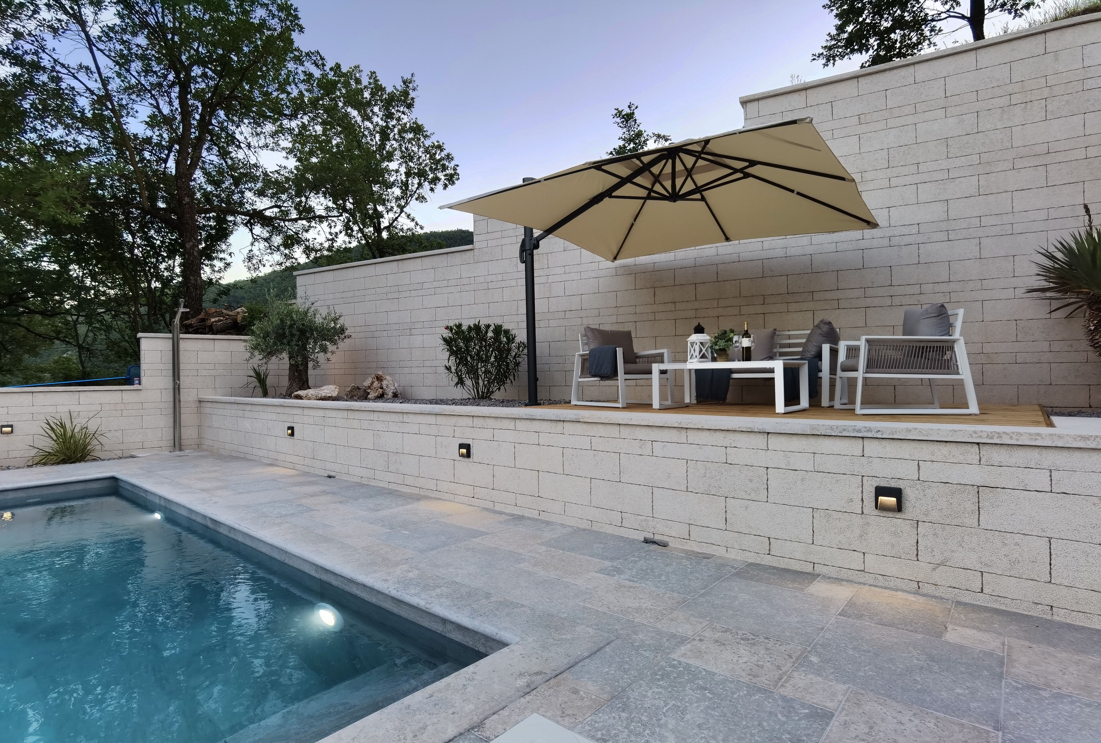 Une piscine avec un espace patio, du mobilier d’extérieur et un grand parasol.