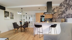 Una cocina moderna con armarios blancos, una isla central y taburetes de bar. Hay un comedor con mesa y sillas.