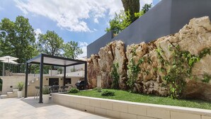 Un patio exterior moderno con pared de piedra, asientos y una pérgola.