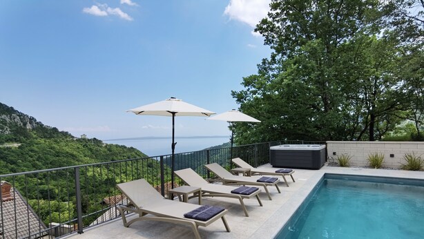 Zona de piscina en la azotea con sillones de descanso y sombrillas, con vistas a un paisaje montañoso.