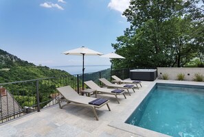 Un espace piscine aménagé sur le toit, avec des chaises longues et des parasols, offrant une vue sur un paysage montagneux.