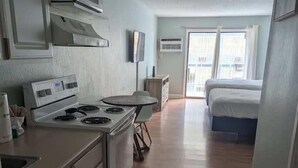 Eine Küche mit Herd, Mikrowelle und Schränken, ein Essbereich mit Tisch und Stühlen sowie ein Schlafzimmer mit Bett und Fenster.