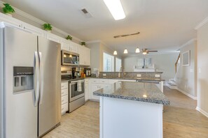 Una cocina moderna con electrodomésticos de acero inoxidable, una isla con encimera de granito y armarios blancos.