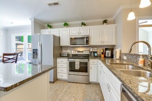 A modern kitchen with white cabinets, granite countertops, stainless steel appliances, and a large island.