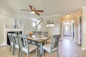 A dining area with a wooden table, chairs, a ceiling fan, and a fireplace.