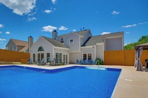 A residential property with a swimming pool, a patio with outdoor furniture, and a large house with multiple windows and a garage.