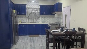 A modern kitchen with blue cabinets, a dining area with a table and chairs, and a living room with a sofa and a coffee table. - Carnbee Cozy Cottage (Carnbee)