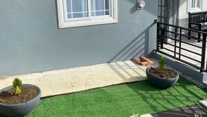 Een balkon met kunstgras, planten in potten, een raam en een leuning.