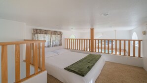 A bedroom with a bed, a wooden railing, a window with curtains, and a view of a pool. - Strawhouse Resorts on the Beautiful Trinity River (Big Flat)