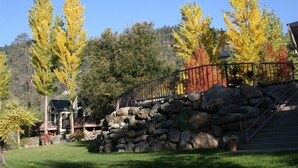 A stone staircase leading up to a wooden deck with a metal railing, surrounded by trees with autumn foliage. - Strawhouse Resorts on the Beautiful Trinity River (Big Flat)