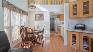 A spacious kitchen with wooden cabinets, a dining area with a wooden table and chairs, and a loft bedroom with a wooden railing. - Strawhouse Resorts on the Beautiful Trinity River (Big Flat)