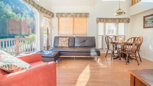 A spacious living area with a leather sofa, a dining table with chairs, and large windows with blinds. - Strawhouse Resorts on the Beautiful Trinity River (Big Flat)