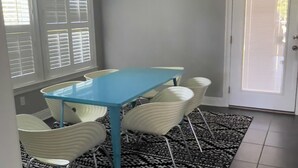 Ein Essbereich mit blauem Tisch, weißen Stühlen, einem gemusterten Teppich und einer Kristallleuchter.