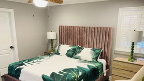 Ein Schlafzimmer mit einem Bett, einem Nachttisch, einem Sessel und einem Fenster mit Jalousien.