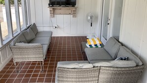 Eine überdachte Veranda mit Korbmöbeln, einem an der Wand befestigten Fernseher und einem Ventilator.