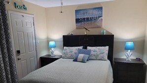 A bedroom with a bed, two bedside tables, a nightstand, a door, and a wall with a motivational quote. - 4-Person Condo only a short walk to beach. (Destin)