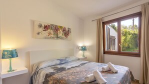 Une chambre à coucher avec un lit, deux lampes de chevet, une fenêtre avec des rideaux et un tableau floral accroché au mur.