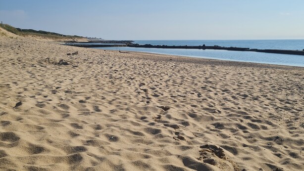 Ein Sandstrand mit Fußspuren und einem ruhigen Meer im Hintergrund.