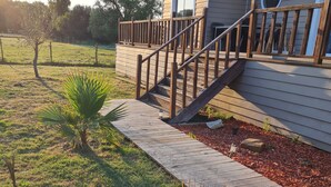 Ein Haus mit einer Holzterrasse, einer Treppe zu einer Veranda und einem kleinen Garten mit Palmen.