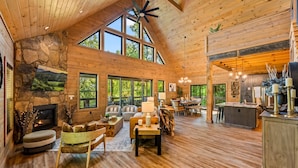 A spacious wooden cabin with a stone fireplace, large windows, and a cozy living area with furniture. - Playground|Views|Pets |Pool |Sauna |Massage Chair (Sevierville)