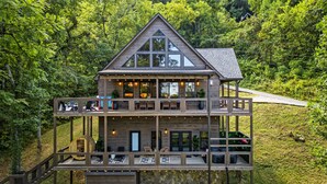 A two-story wooden cabin with a balcony, surrounded by lush greenery. - Playground|Views|Pets |Pool |Sauna |Massage Chair (Sevierville)
