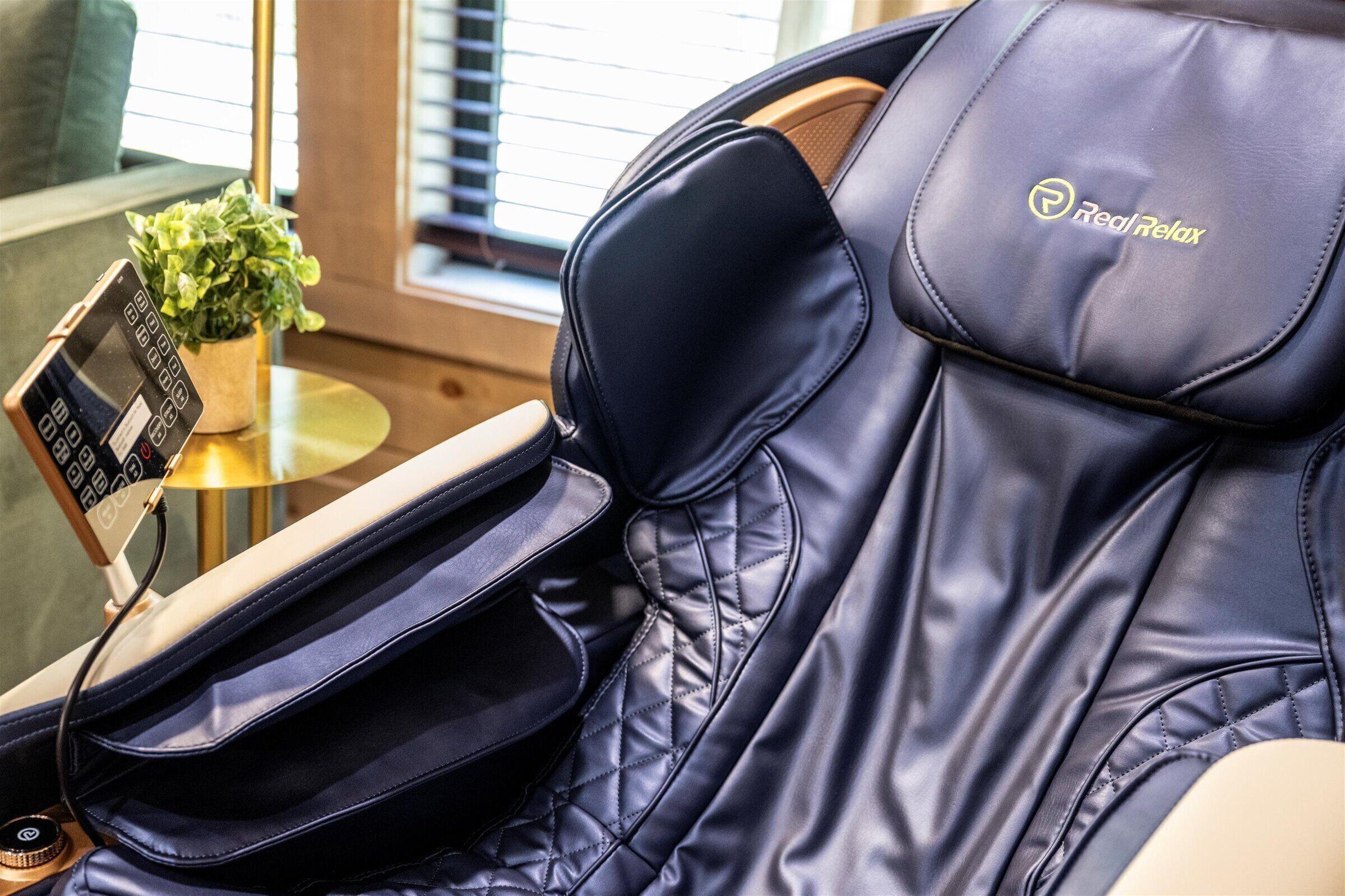 A massage chair with a control panel and a small potted plant on a side table.
