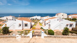 A coastal residential area with white buildings, a paved pathway, and a view of the sea. - Rimar 4, 2 bedroom apartment, Cap d´Artrutx (Cala´n Bosch)