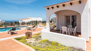 A pool area with lounge chairs and a table, a covered patio with a table and chairs, and a view of the sea. - Rimar 4, 2 bedroom apartment, Cap d´Artrutx (Cala´n Bosch)