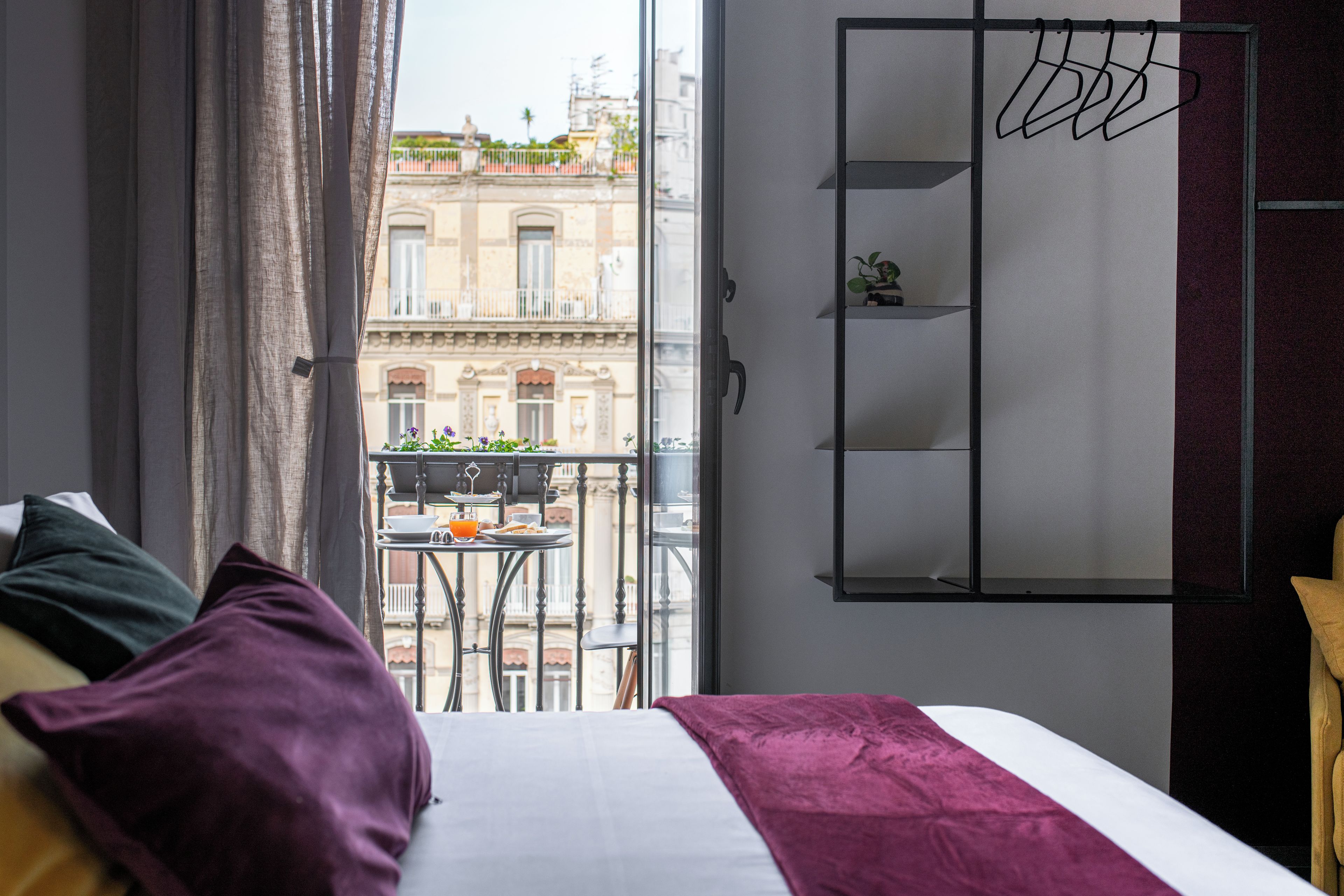 A hotel room with a bed, a balcony with a table and chairs, and a view of a building with balconies.