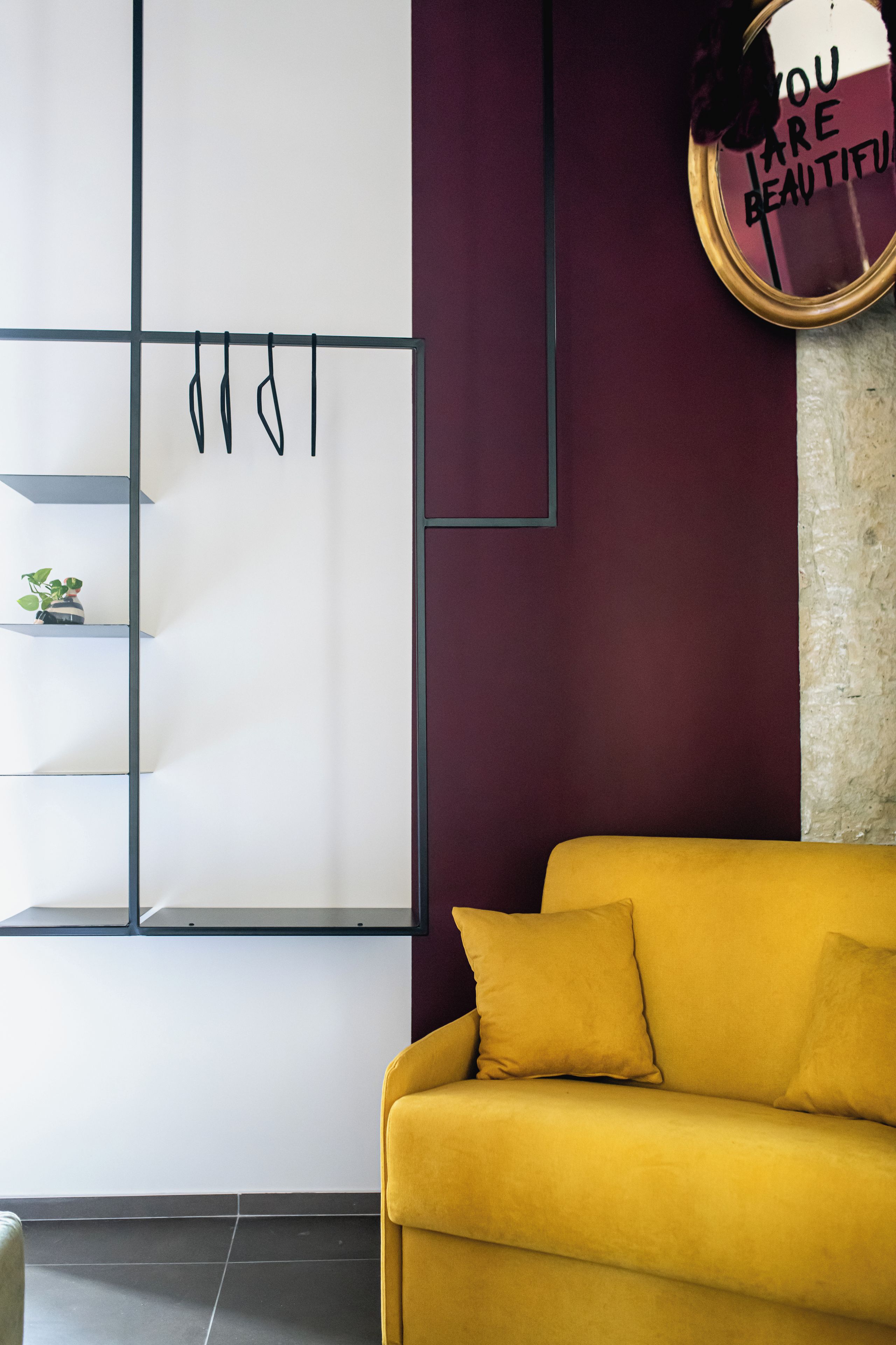 Ein Zimmer mit einem gelben Sofa, einer Wandablage mit Haken und einem dekorativen Schild.