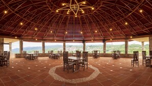 An open-air dining area with stone walls, wooden tables and chairs, and a view of the landscape. - Villa de los Vientos (Cuetzalan del Progreso)