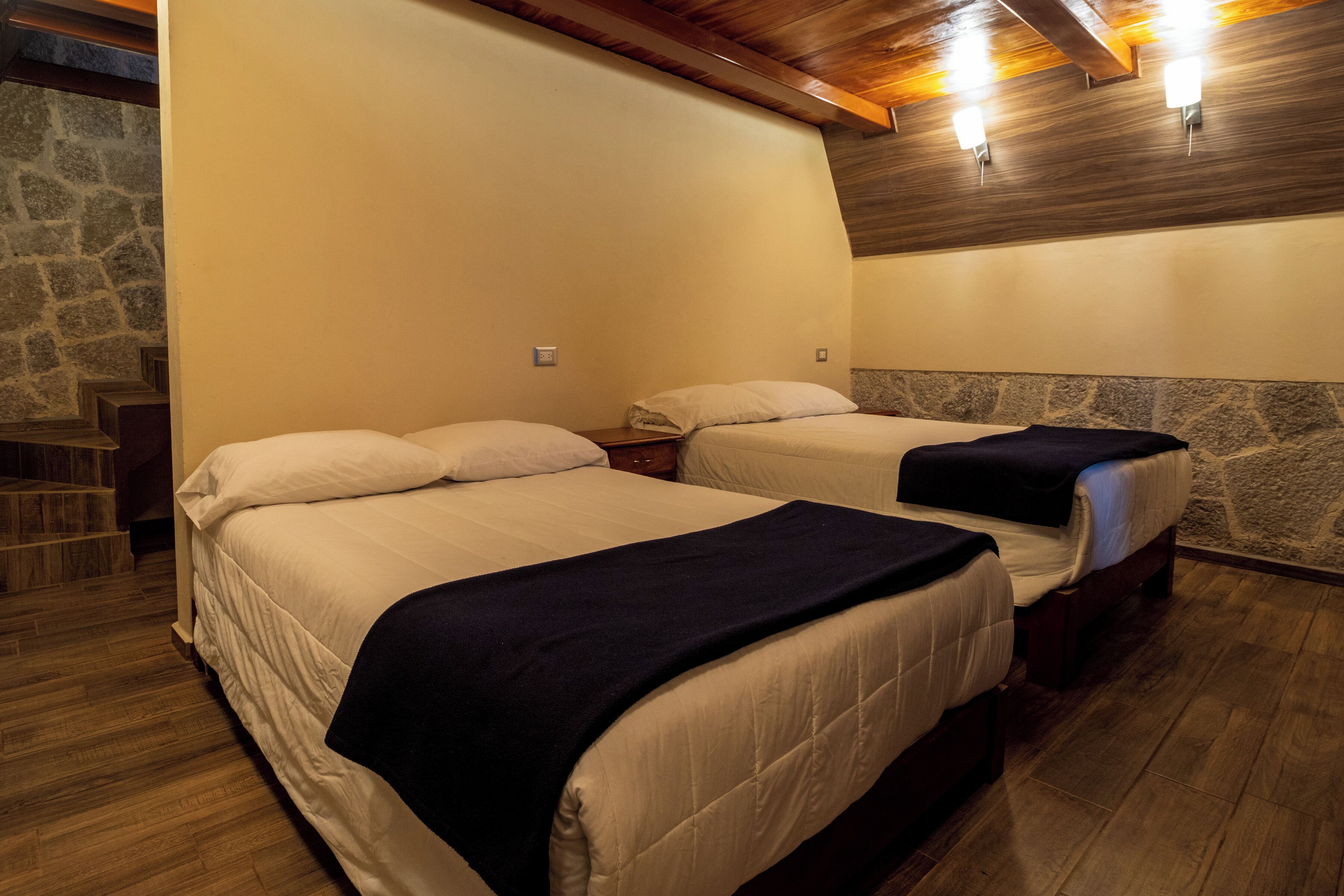 A hotel room with two beds, wooden flooring, stone wall accents, and built-in lighting.