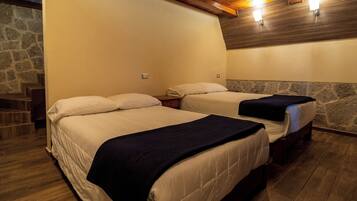 A hotel room with two beds, wooden flooring, stone wall accents, and built-in lighting.