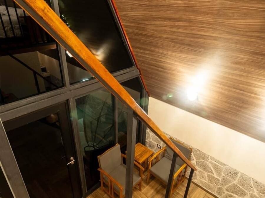 Un intérieur moderne avec un escalier en bois, un mur en pierre et une porte en verre donnant sur une autre pièce.