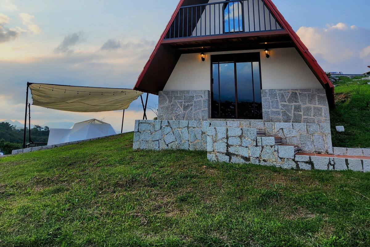 Una casa moderna con base de piedra, techo rojo y un balcón.