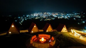 A night view of a resort with multiple conical-roofed cabins and a central fire pit area. - Villa de los Vientos (Cuetzalan del Progreso)