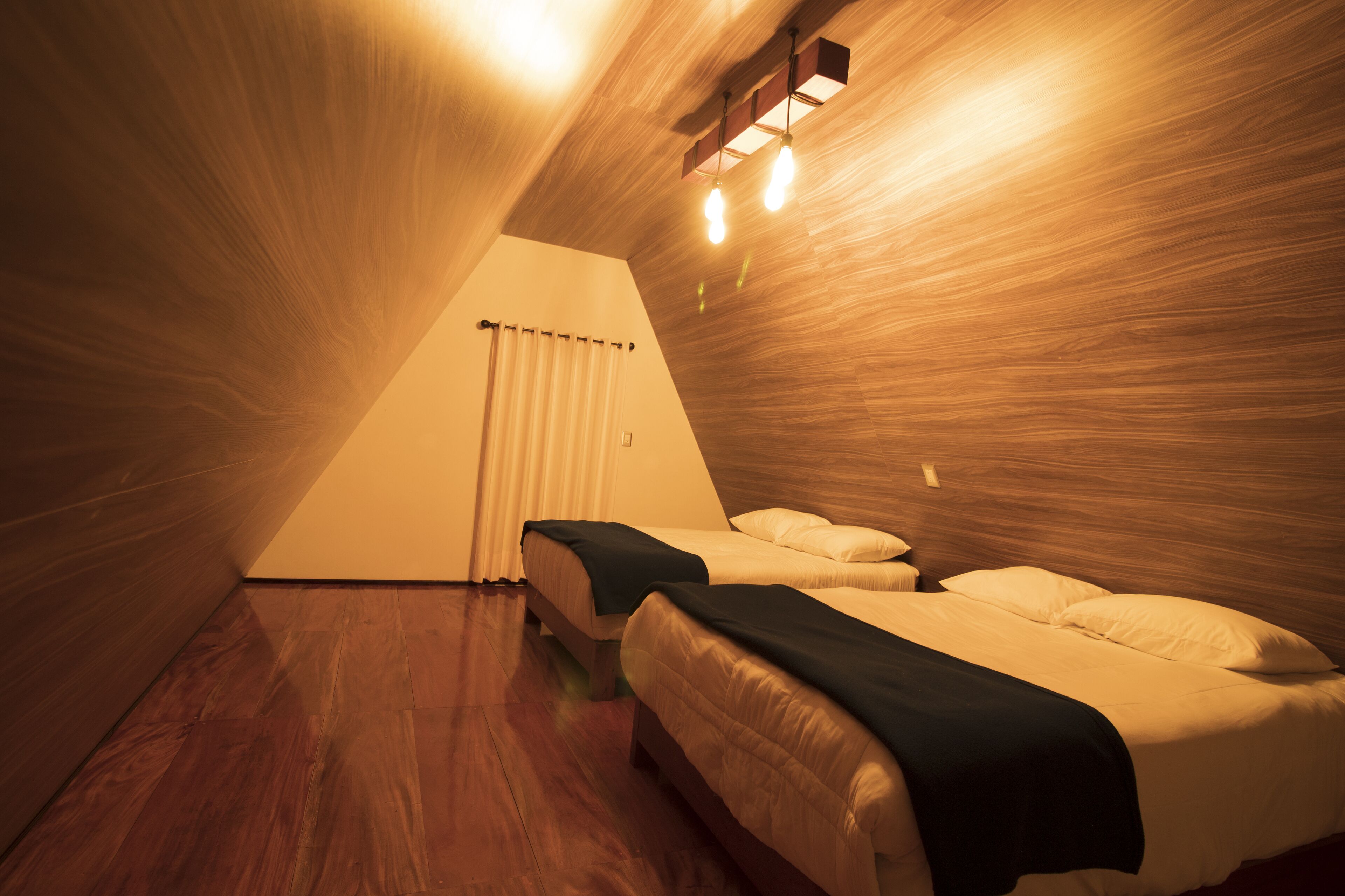 Ein raumförmiger Bereich in Dreiecksform mit zwei Betten, Holzwänden und einer geneigten Decke.