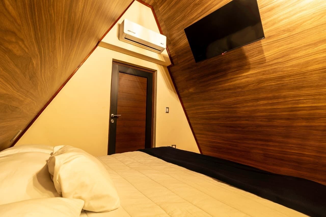A triangular room with a bed, a door, and an air conditioning unit.