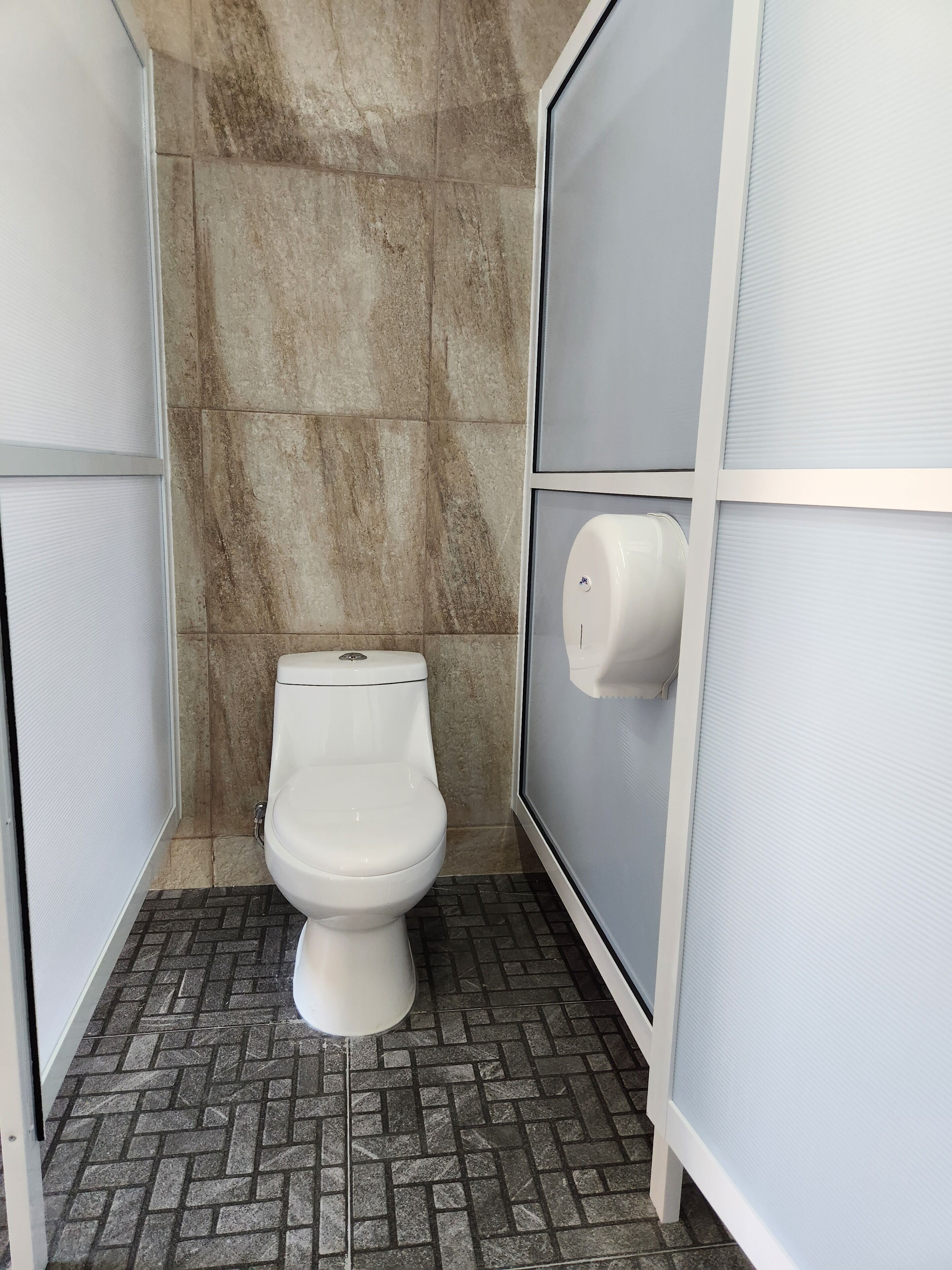 A small, private bathroom with a toilet, a hand dryer, and a tiled floor.