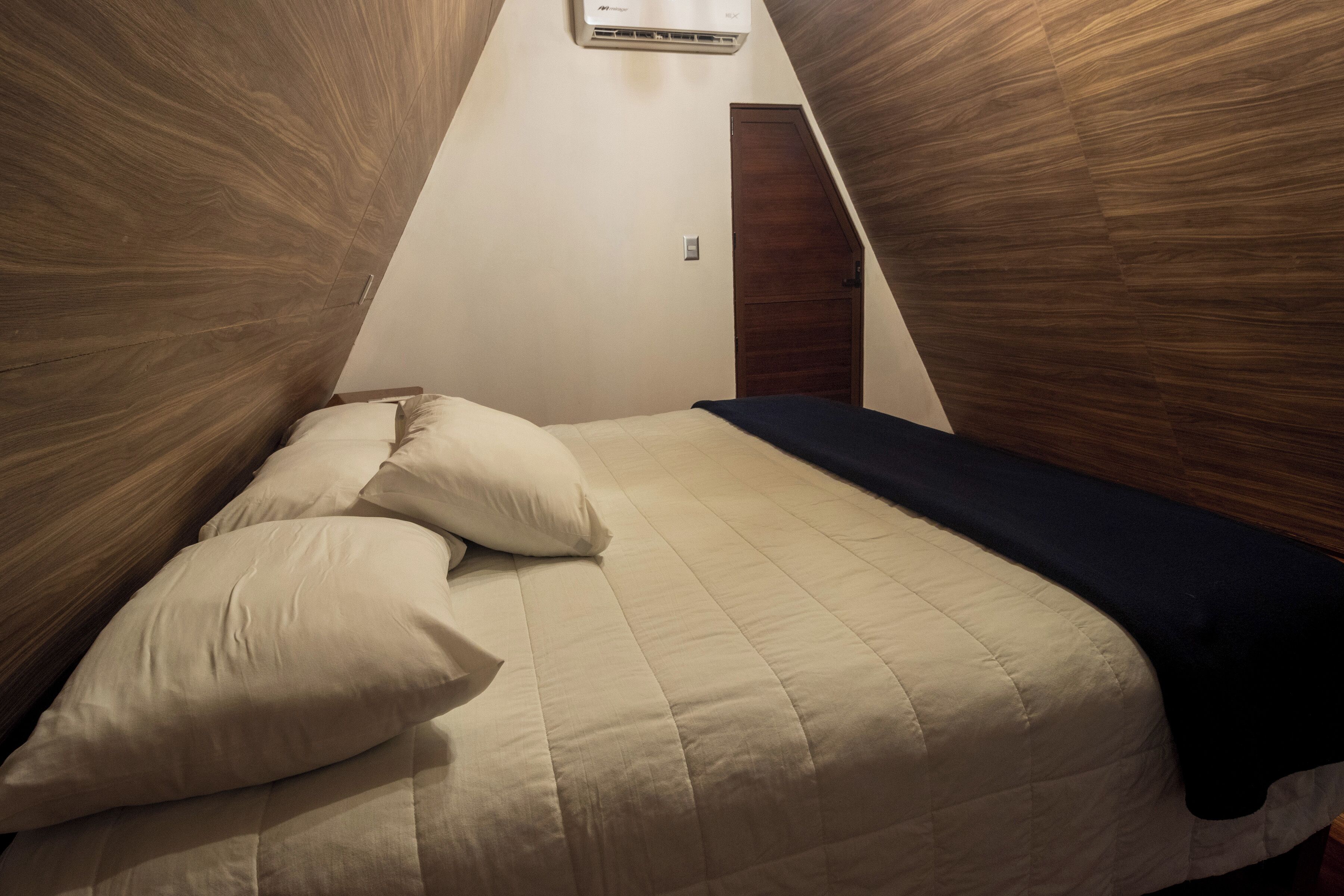 Un dormitorio con techo inclinado, una cama con cubrecama acolchado y una puerta de madera.