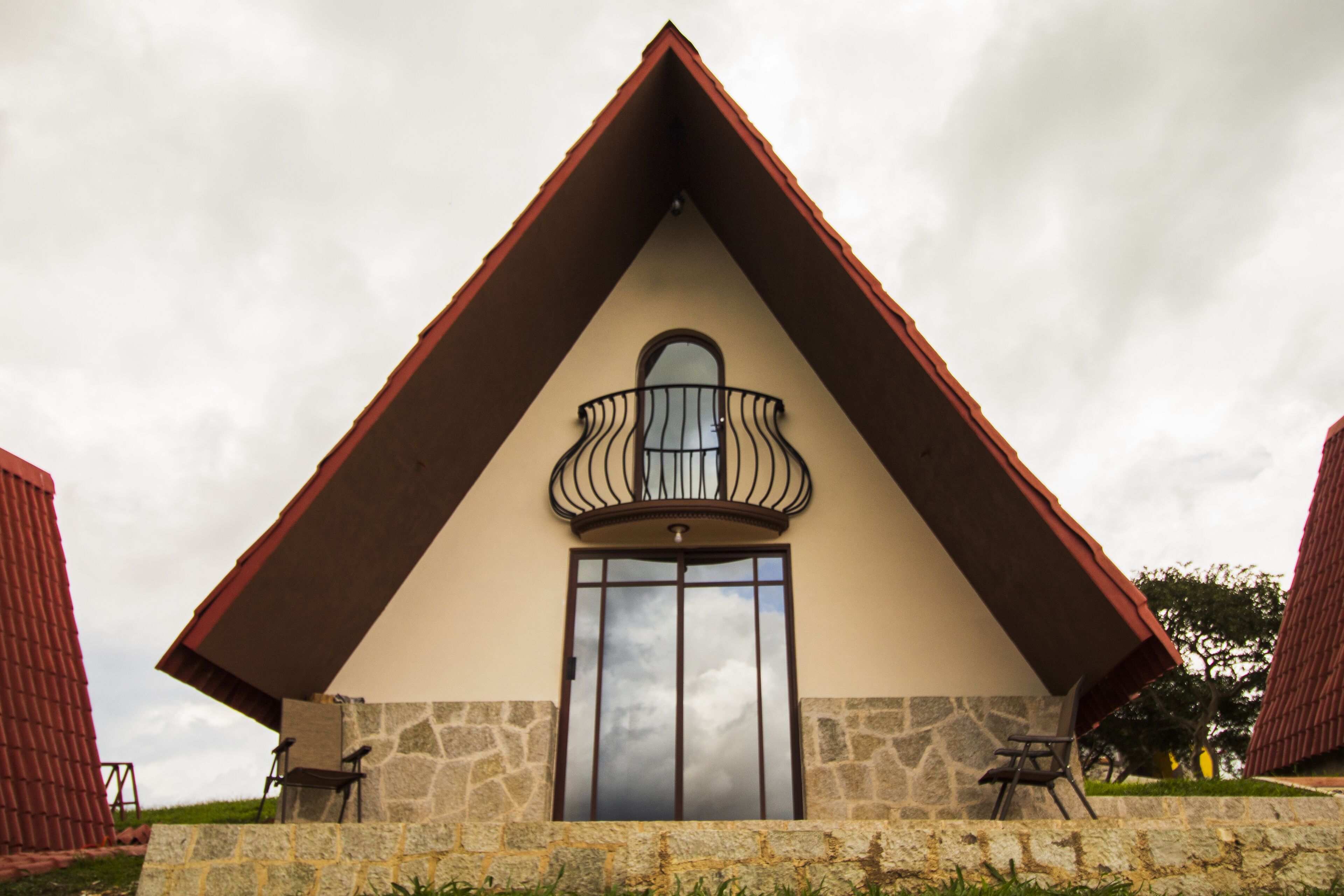 A building with a triangular roof, a balcony with a metal railing, and a large window.