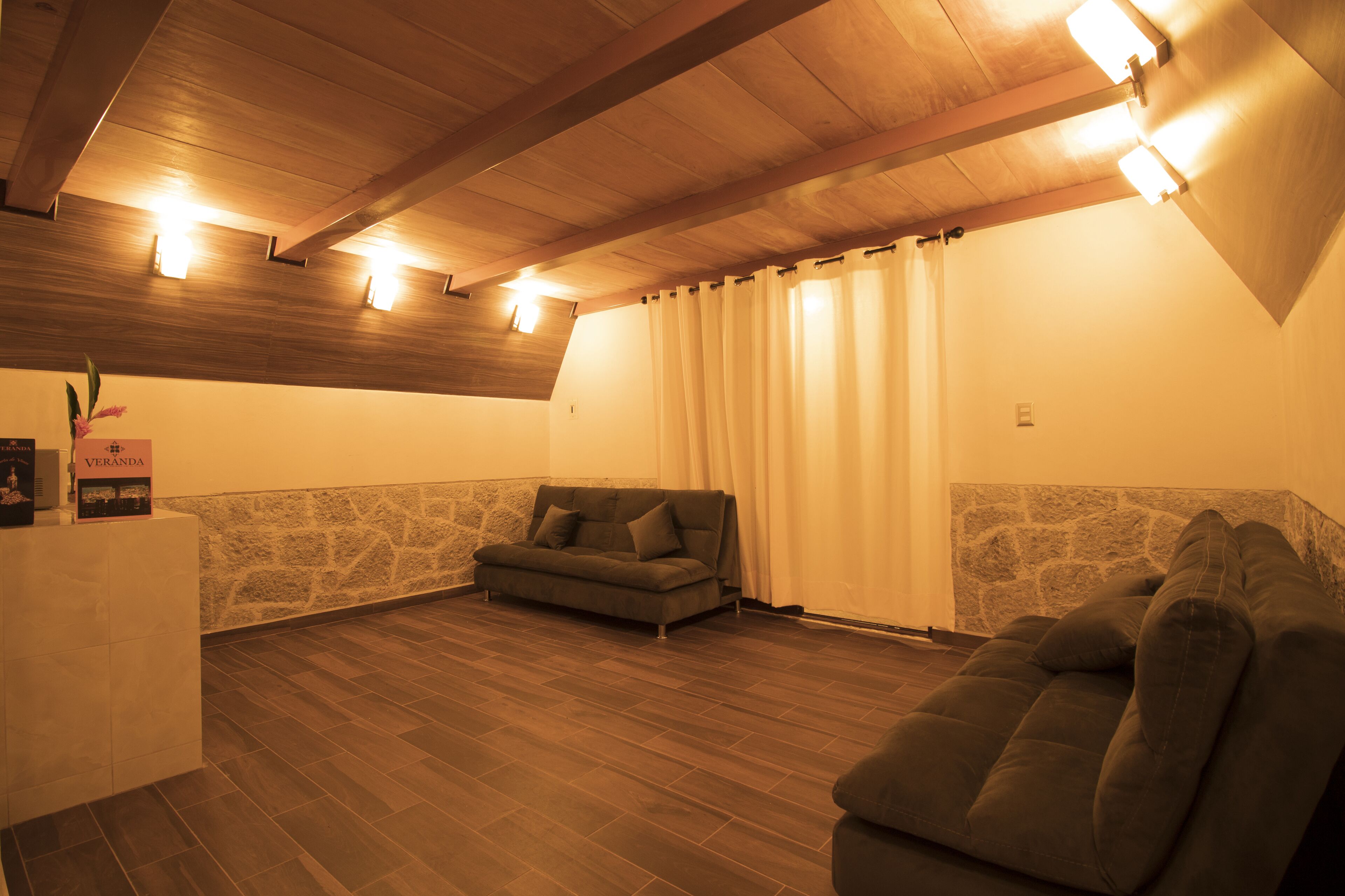 Ein gemütlicher Raum mit Holzbalkendecke, einer Wand aus Stein und einer Sitzecke mit Sofa und gepolstertem Sitzbrett.