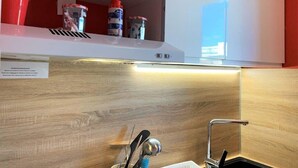 Een keuken met een houten spatwand, een roestvrijstalen spoelbak en een wit kastje erboven met rode bekers en bakjes.