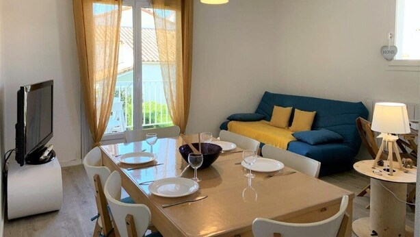 Een eethoek met een houten tafel gedekt voor vier personen, een televisie op een standaard en een bank met kussens.