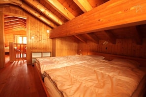 A wooden cabin interior with a large bed, wooden walls, and a sloped ceiling.