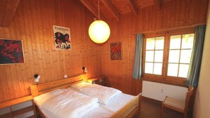 Una habitación de cabaña de madera con una cama, un banco y una ventana con cortinas.